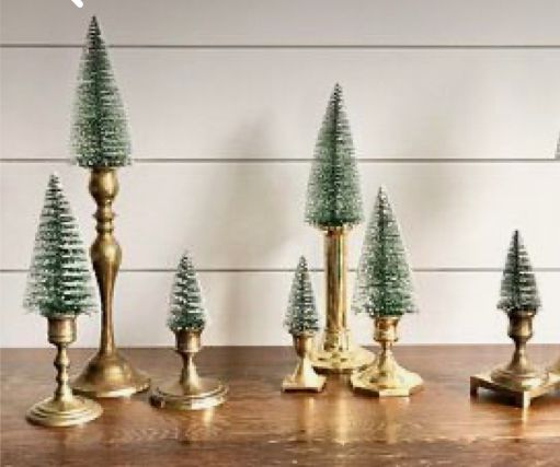 small christmas trees are lined up next to candlesticks on a wooden table in front of a white wall