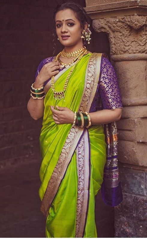 a woman in a green and purple saree standing next to a stone wall with jewelry on it