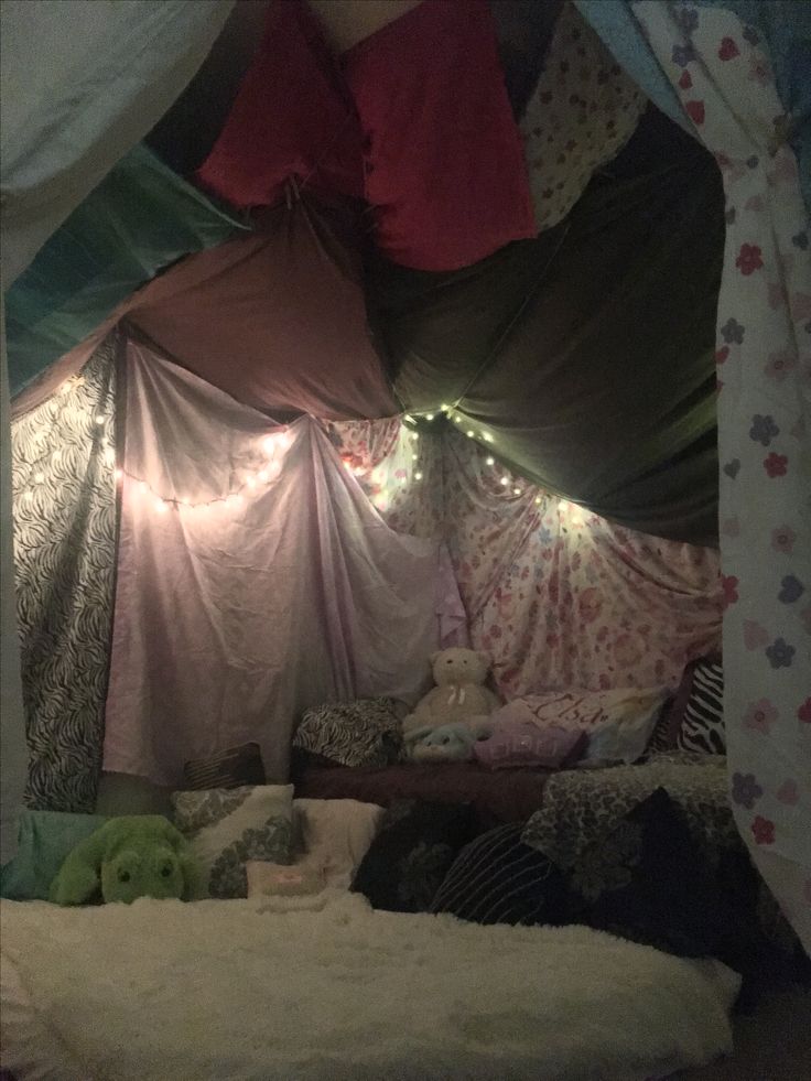 a bed covered in lots of pillows and blankets with lights on the top of it