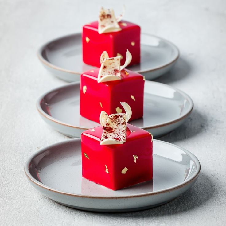 three plates with red desserts on them sitting next to each other in the shape of cubes