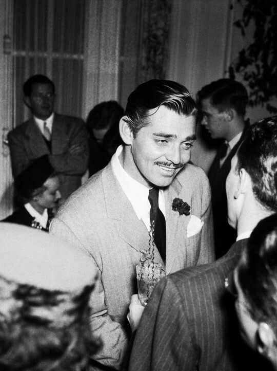 a black and white photo of a man in a suit talking to some other people