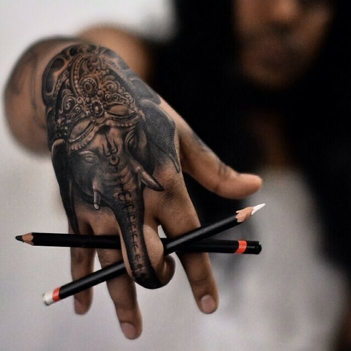 a person holding two pencils in their hand and an elephant tattoo on the other hand