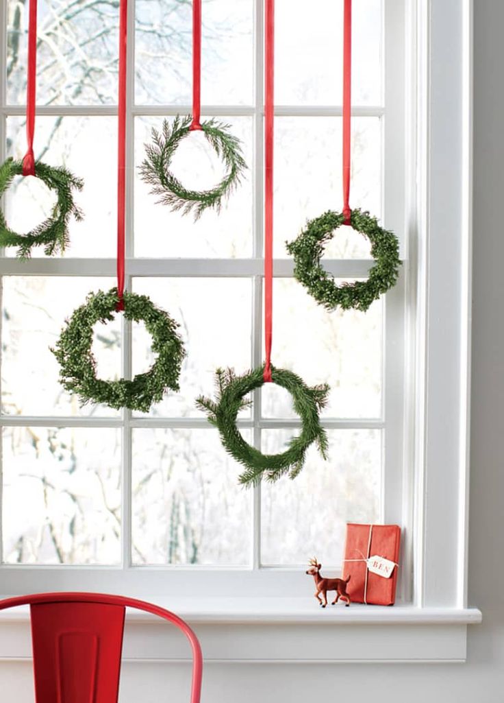 christmas wreaths hanging on the window sill in front of a red chair and table