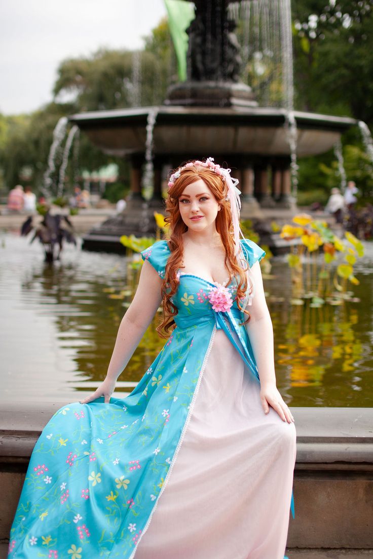 a woman in a blue and pink dress standing next to a fountain