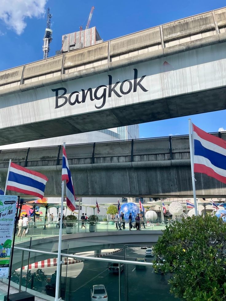 people walking under an overpass with flags in the foreground and a bankkok sign above it