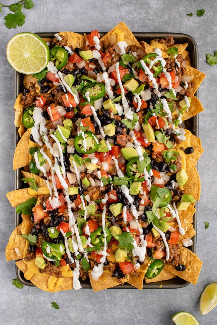 an overhead shot of nachos on a tray with lime wedges