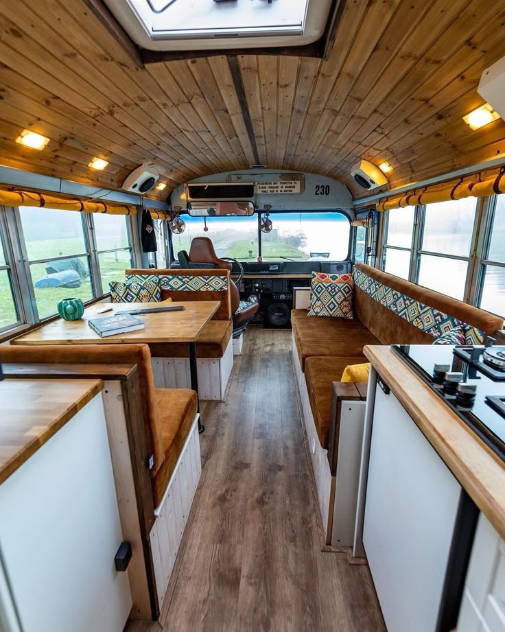 the interior of an rv with wood flooring and white cabinets, windows, and counters