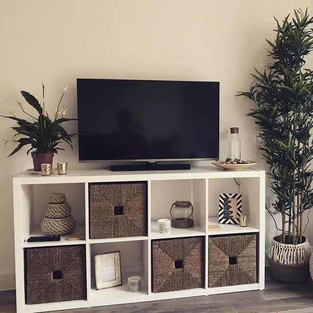 a flat screen tv sitting on top of a white shelf next to baskets and potted plants