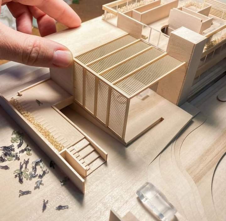 a hand is pointing at a model of a building