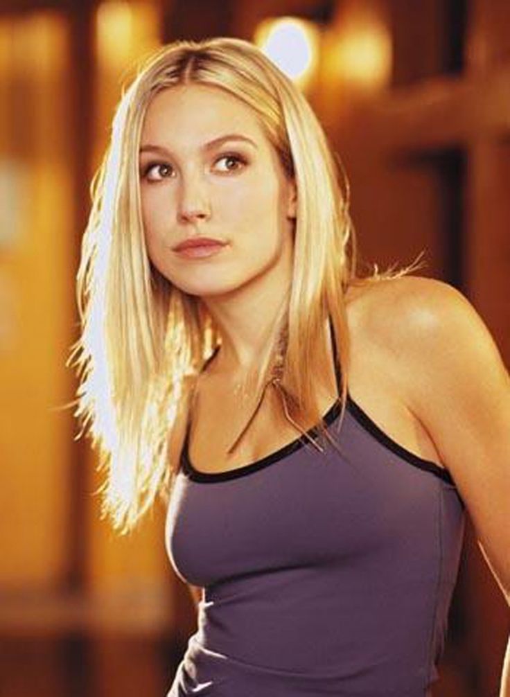 a woman with blonde hair wearing a tank top and looking at the camera while standing in an empty room