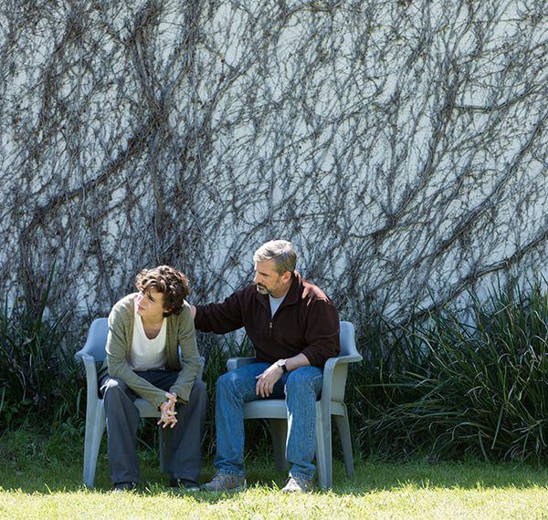 a man and woman sitting on chairs in front of a wall with vines behind them