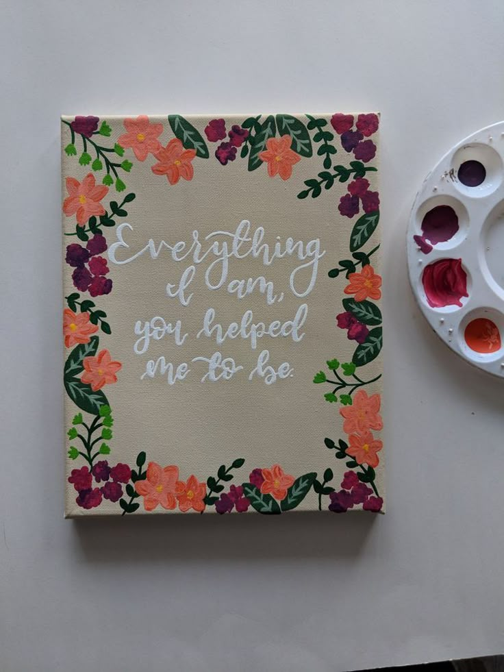 a card with some paint and flowers on it next to a painting brush, palette and watercolors