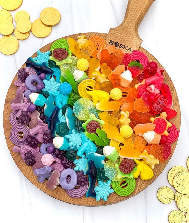 a wooden spoon filled with lots of colorful candies next to some gold coins on a white surface