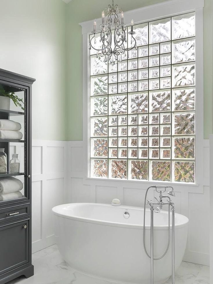 a white bath tub sitting under a window next to a cabinet with towels on it