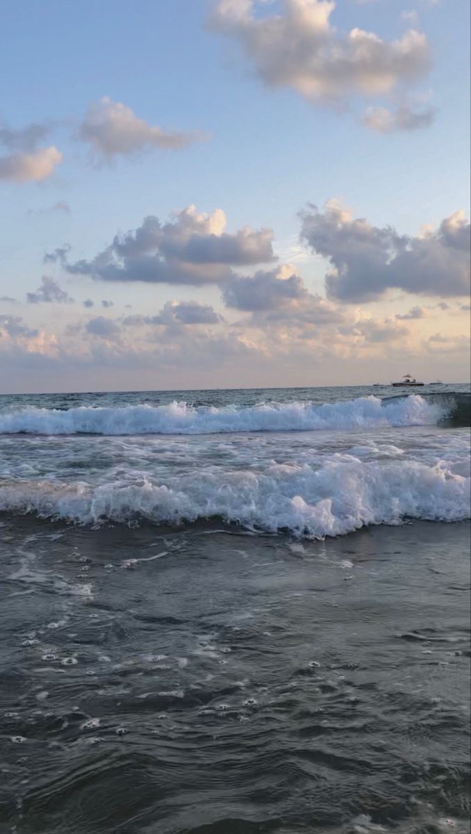 the waves are crashing on the beach in front of the sky with white fluffy clouds