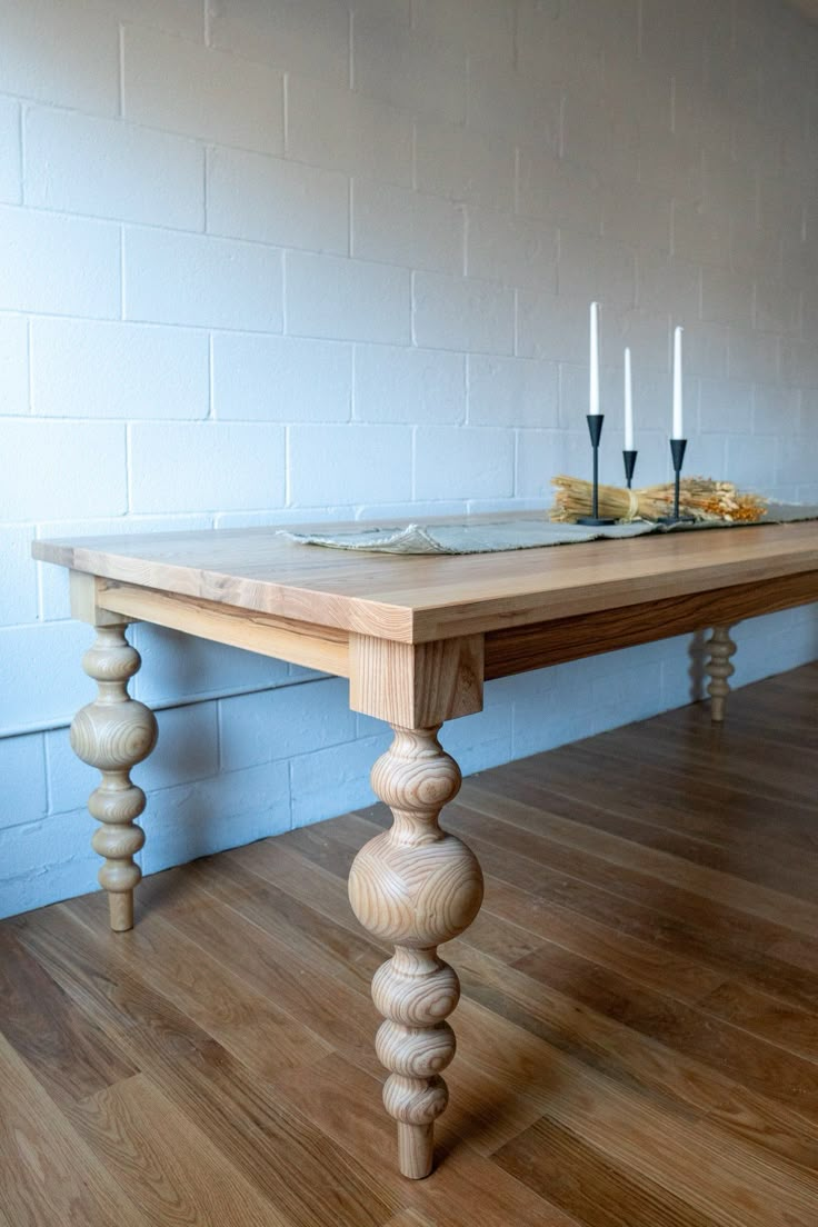 a wooden table sitting on top of a hard wood floor next to a white brick wall