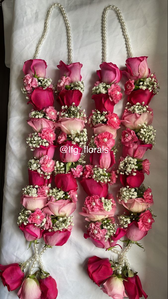 pink roses and baby's breath are arranged on a white sheet with pearl necklaces