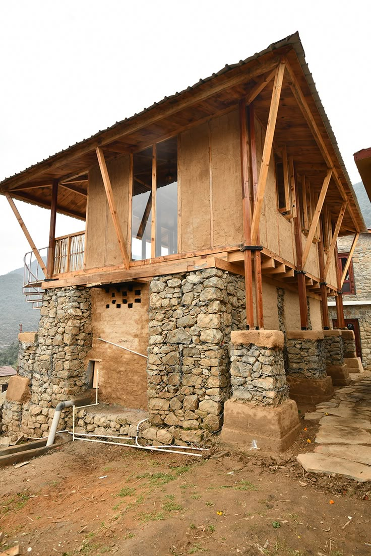 an unfinished house with stone walls and wooden beams on the roof, in front of a mountain range