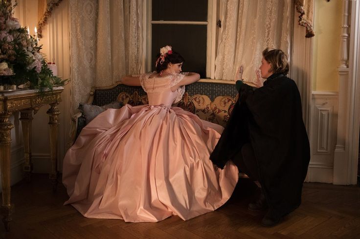 a woman in a pink dress sitting on a couch next to a man wearing a black suit