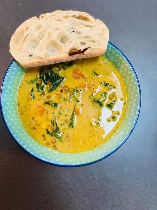 a bowl filled with soup next to a piece of bread on top of a table