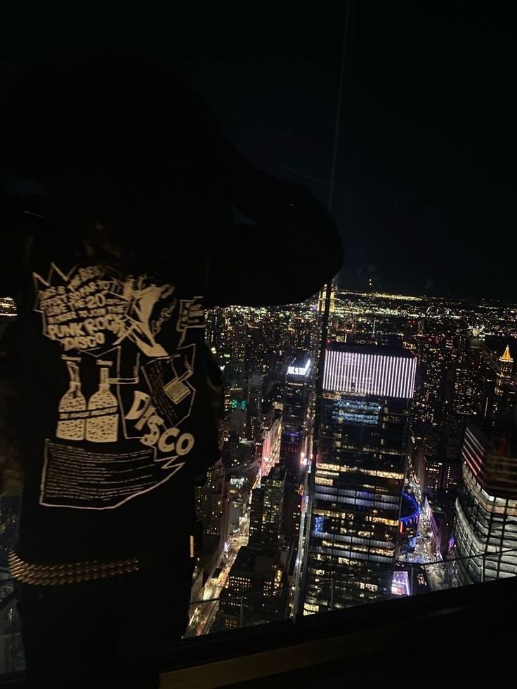 a man standing on top of a tall building looking at the city lights and skyscrapers