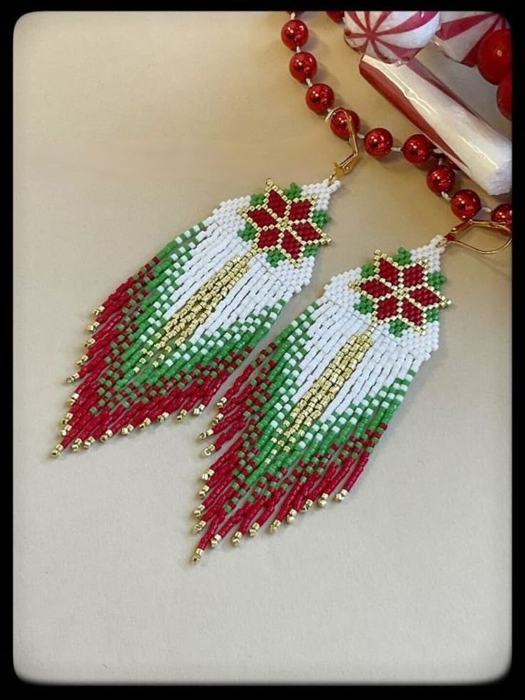 two red and white beaded earrings on a table next to a christmas tree ornament