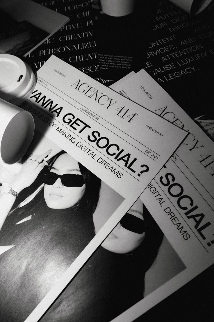 black and white photograph of magazine covers with sunglasses on it's face, next to a coffee cup