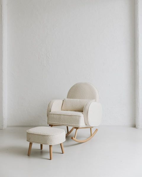 a white rocking chair and footstool in front of a white wall with an open window