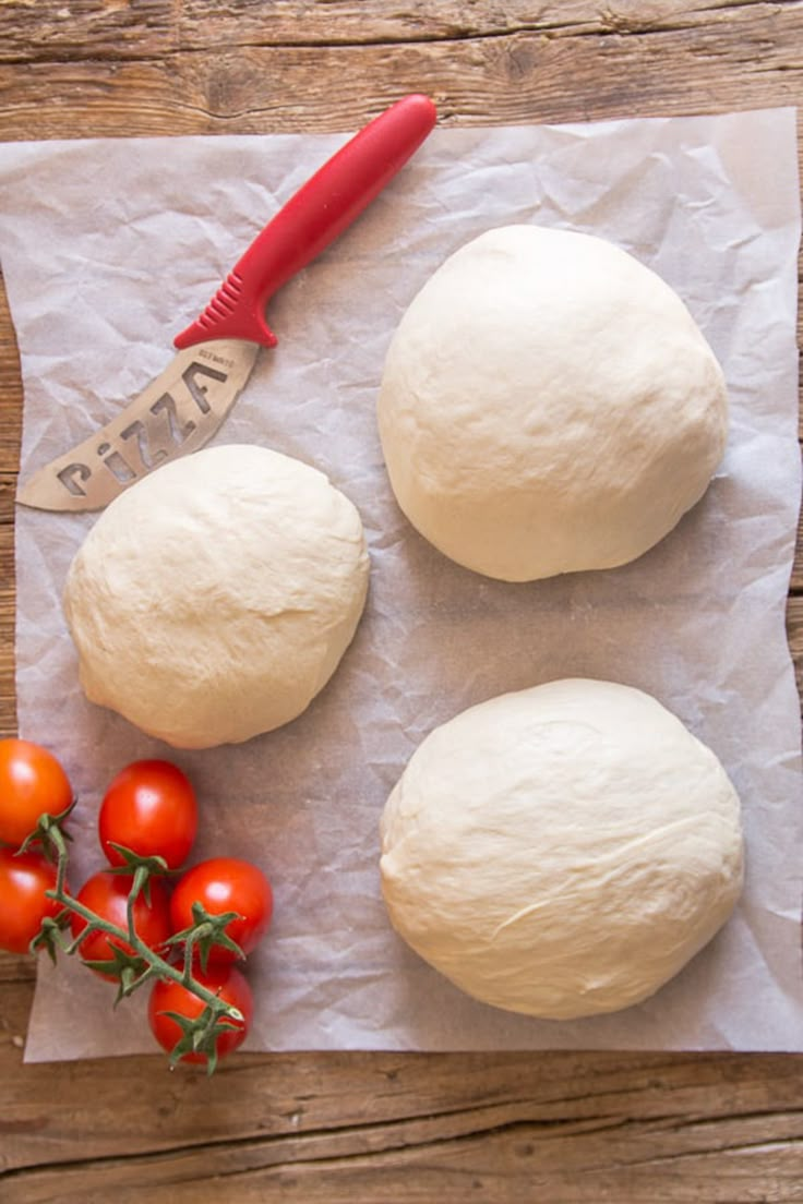 three uncooked buns and tomatoes on a piece of wax paper with a knife