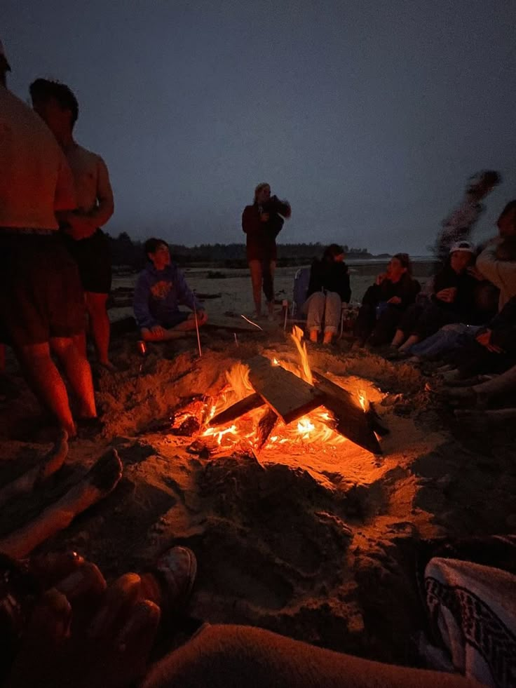 people sitting around a campfire on the beach at night