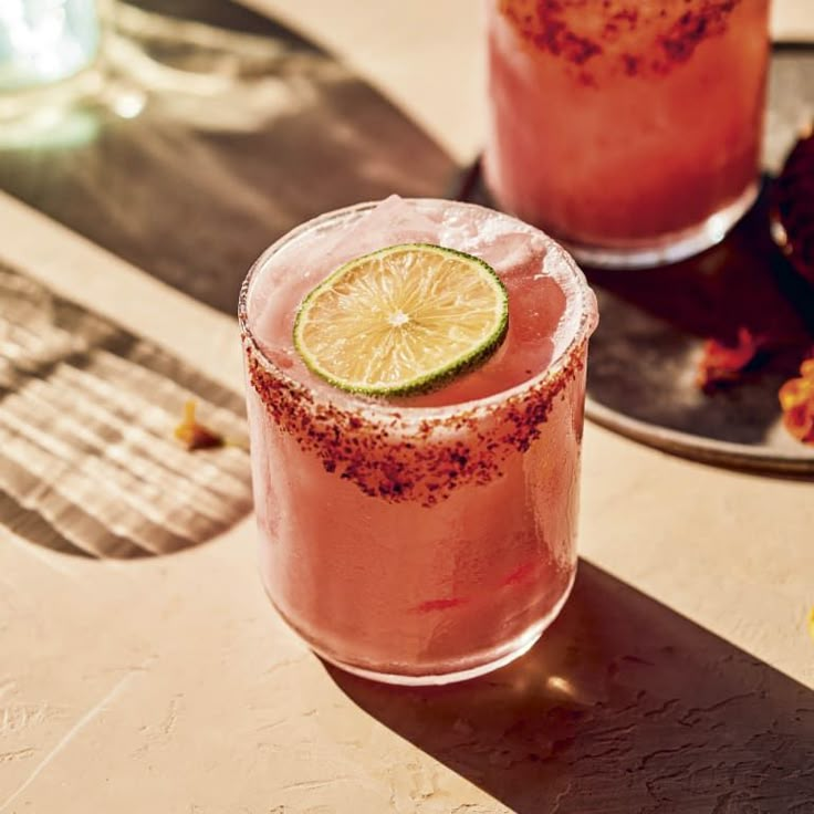 two margaritas sitting on top of a table next to each other, one with a lime