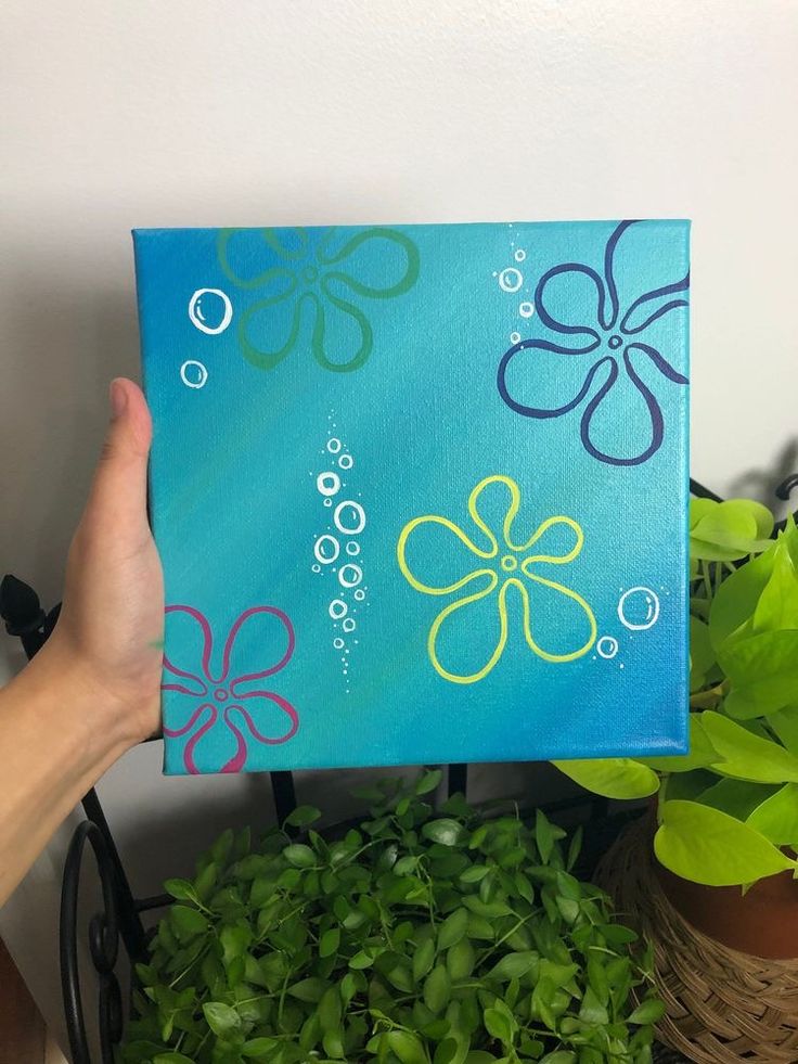 a hand holding up a blue box with flowers painted on it and green plants in the background