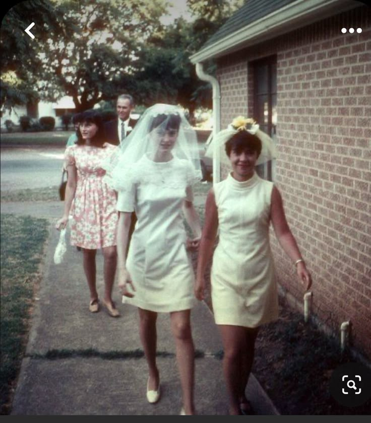 two women in short dresses are walking down the sidewalk with one woman wearing a veil