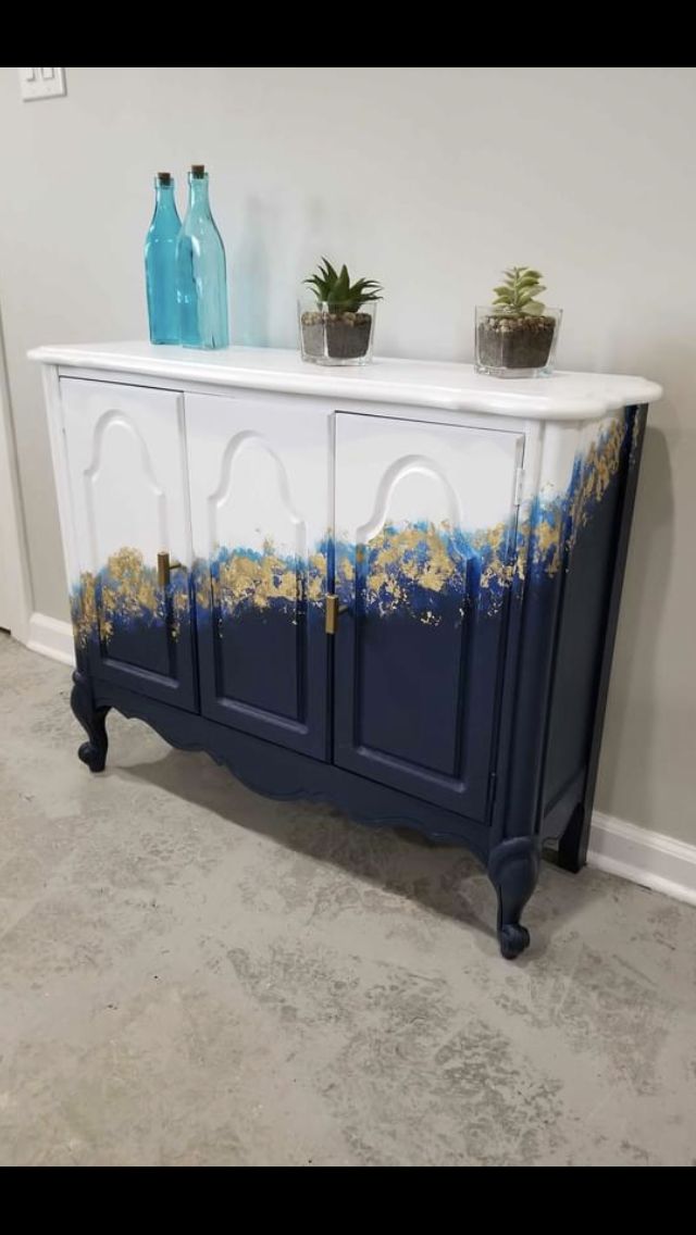 a blue and white cabinet with gold paint on the top, next to two vases