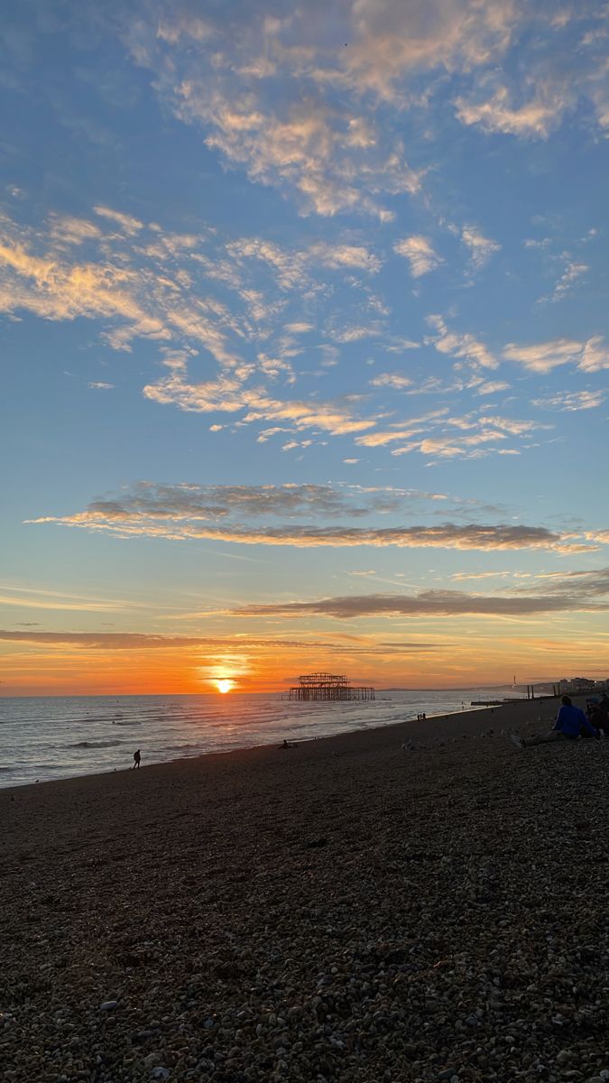 the sun is setting at the beach with people on it