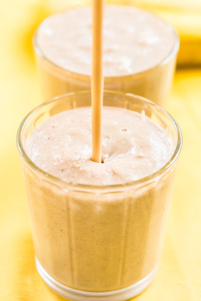 two glasses filled with smoothie on top of a yellow cloth covered table next to bananas