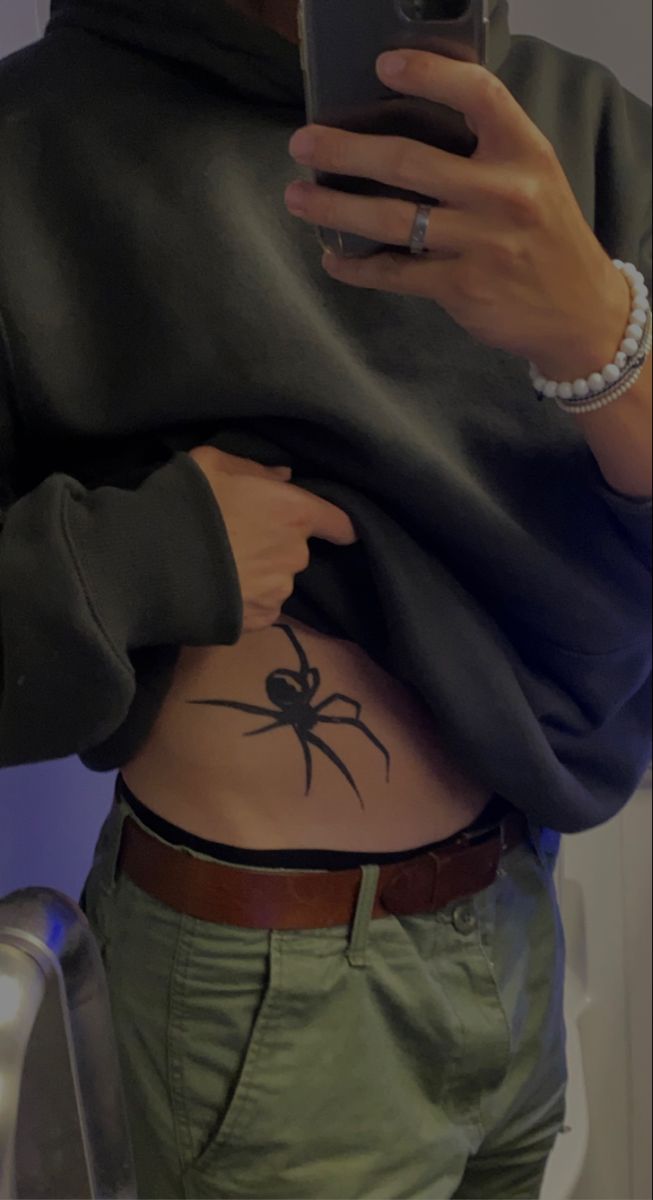 a person with a spider tattoo on their stomach holding a cell phone and taking a selfie