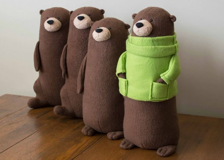 three stuffed bears are standing next to each other on a wooden table and one is wearing a green sweater