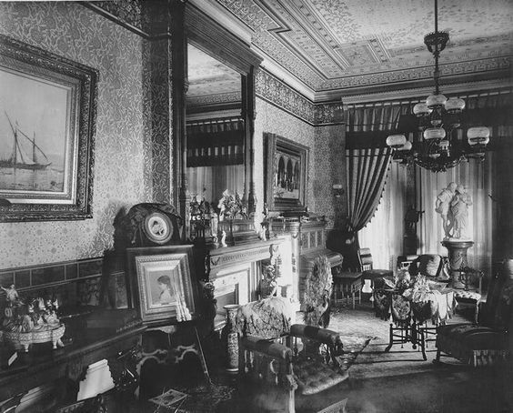 an old black and white photo of a living room with antique furniture, paintings on the walls