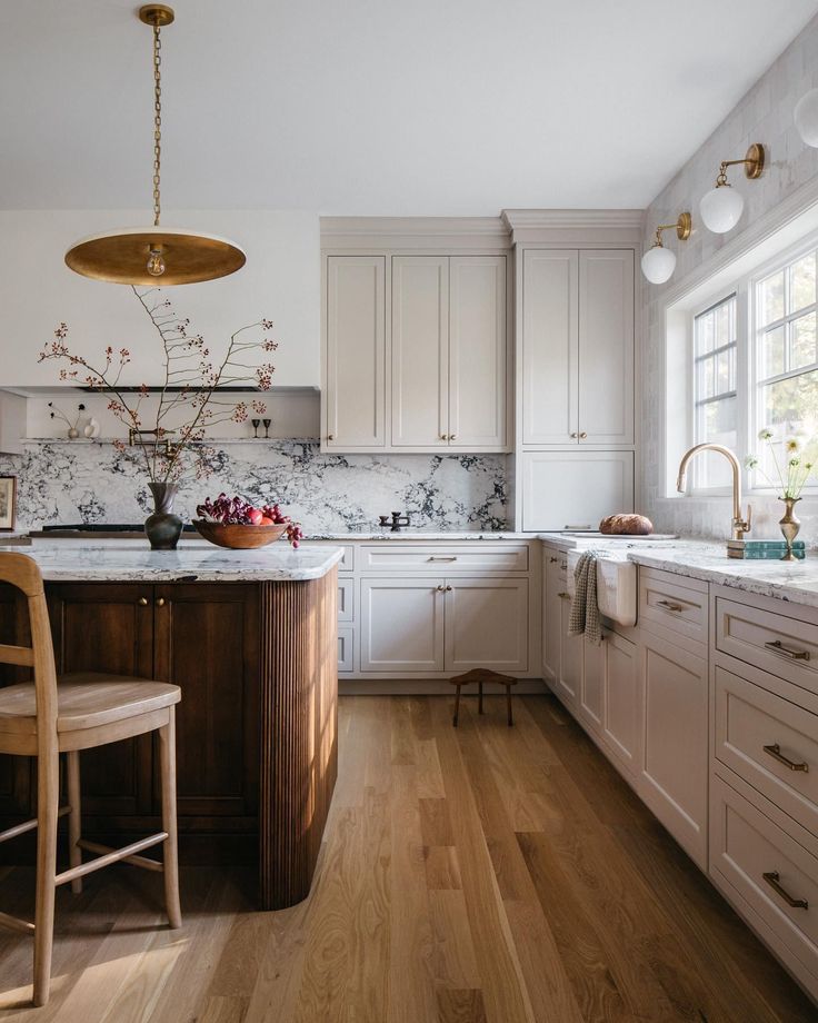 a kitchen with white cabinets and wood floors, an island countertop and chairs in front of the window