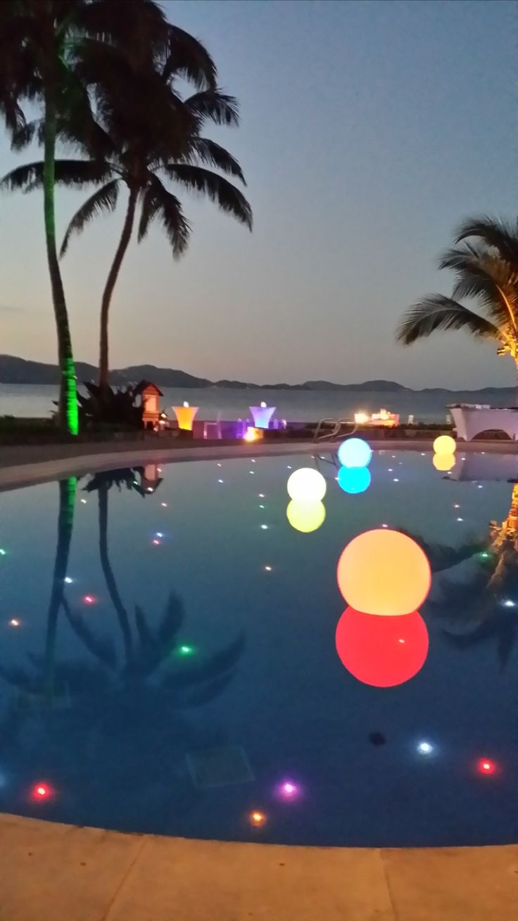 an outdoor pool with colorful lights and palm trees