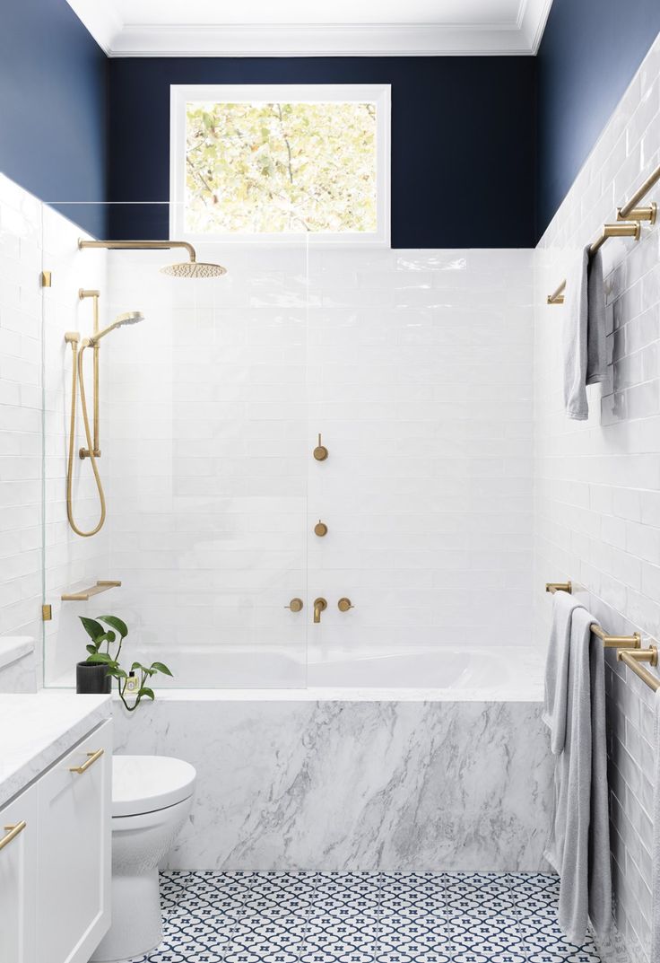 a bathroom with blue and white walls, tile flooring and gold fixtures on the shower