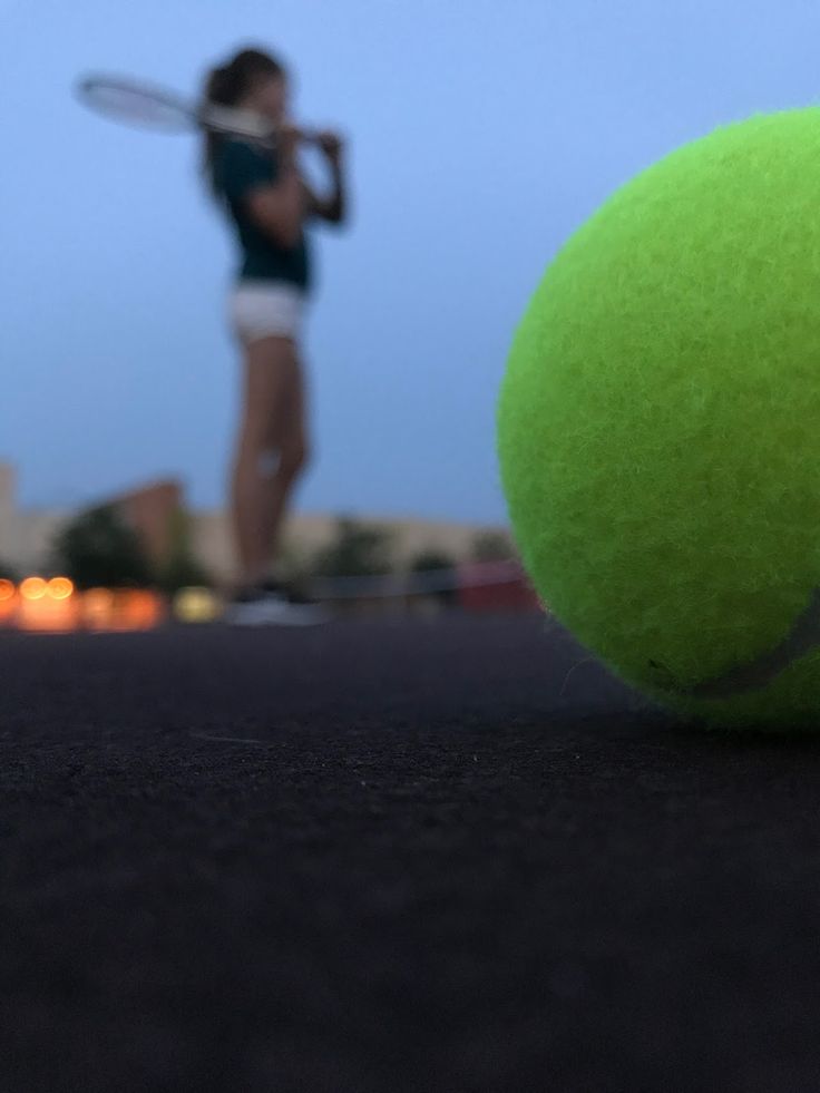 a tennis ball on the ground with a person in the background holding a racket