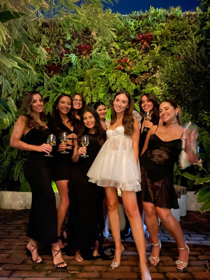 a group of women standing next to each other in front of a lush green wall