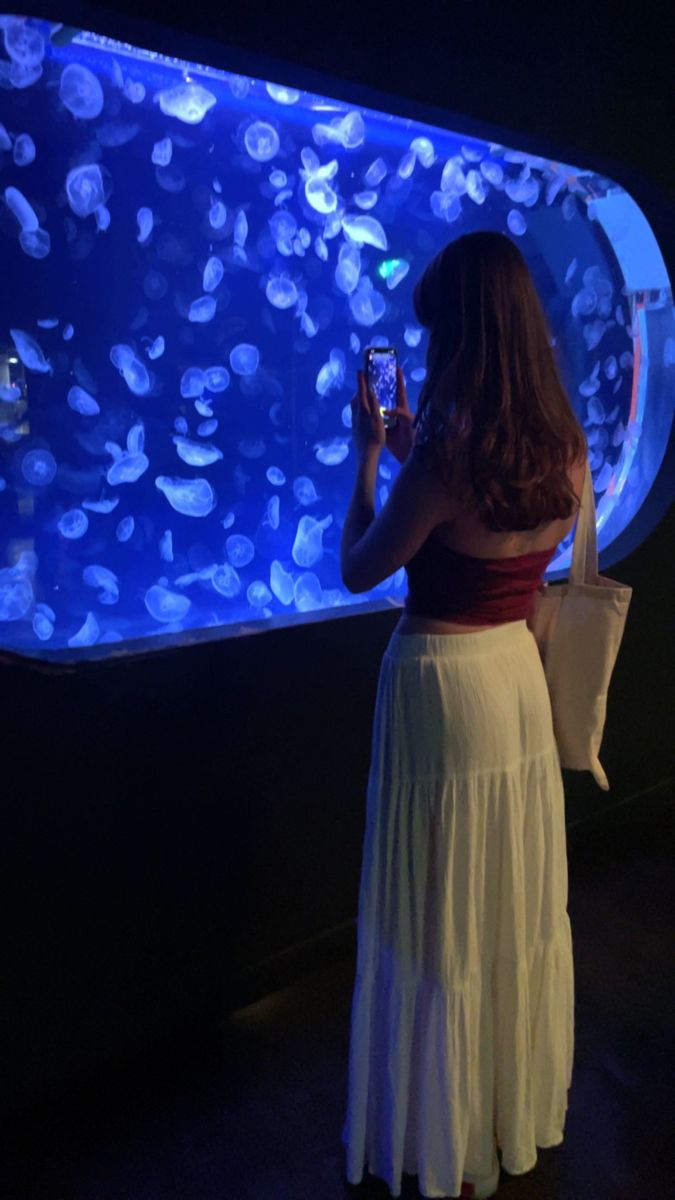 a woman standing in front of an aquarium looking at her cell phone