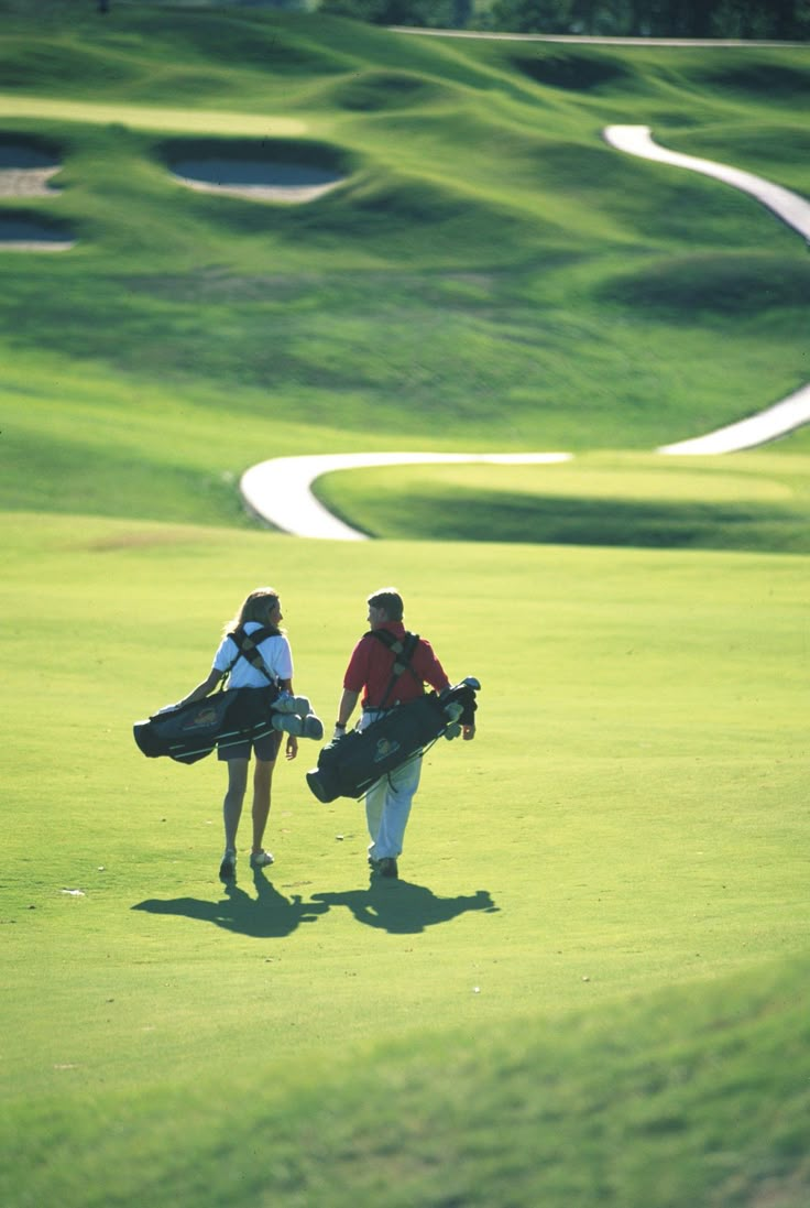 two people walking on a golf course carrying their gear and bags to the next hole