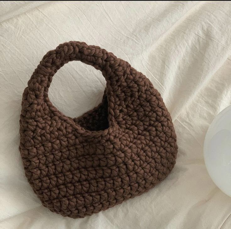 a brown crocheted bag sitting on top of a bed