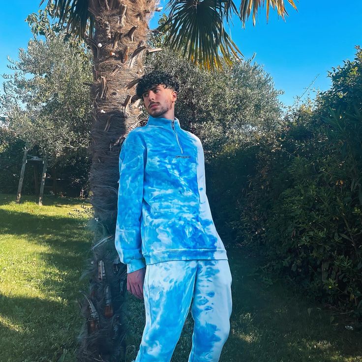 a man standing in front of a palm tree wearing blue tie - dyed tracksuits