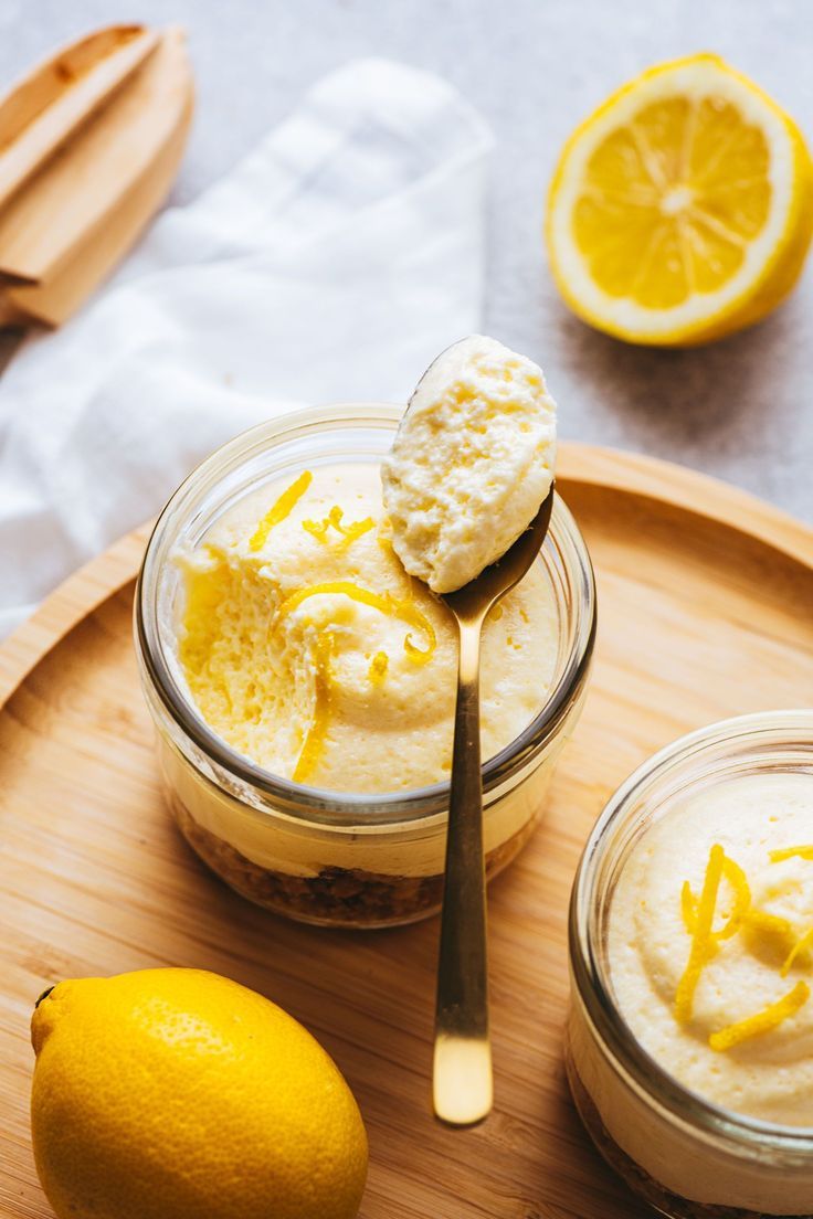 two jars with lemon custard and whipped cream on a wooden tray next to sliced lemons