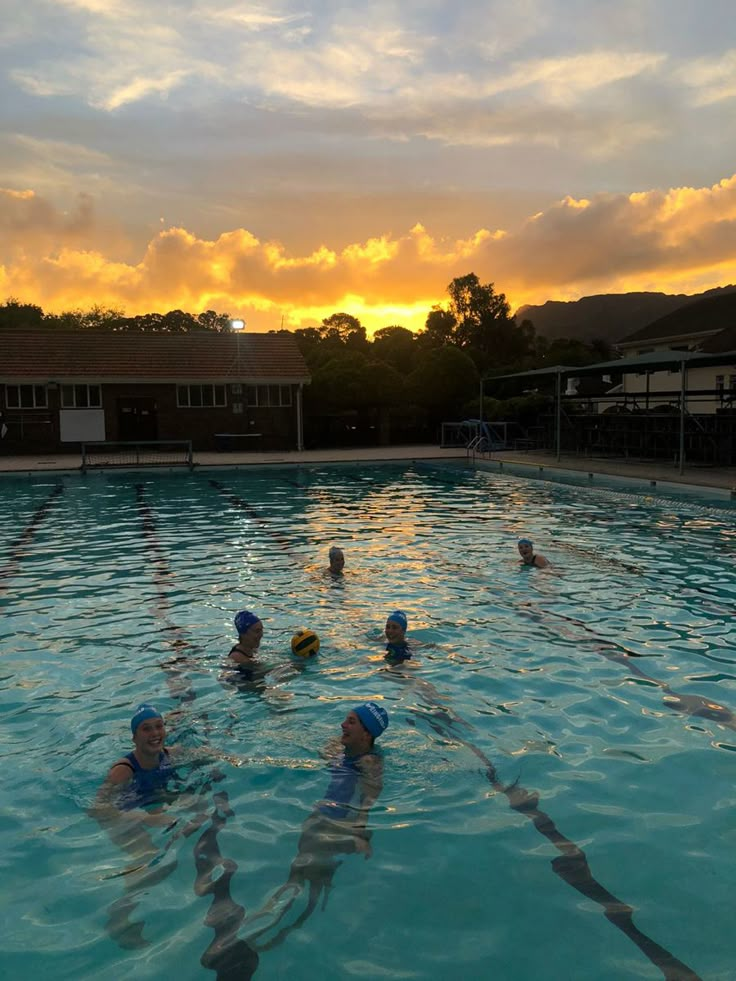 several people are swimming in the pool at sunset